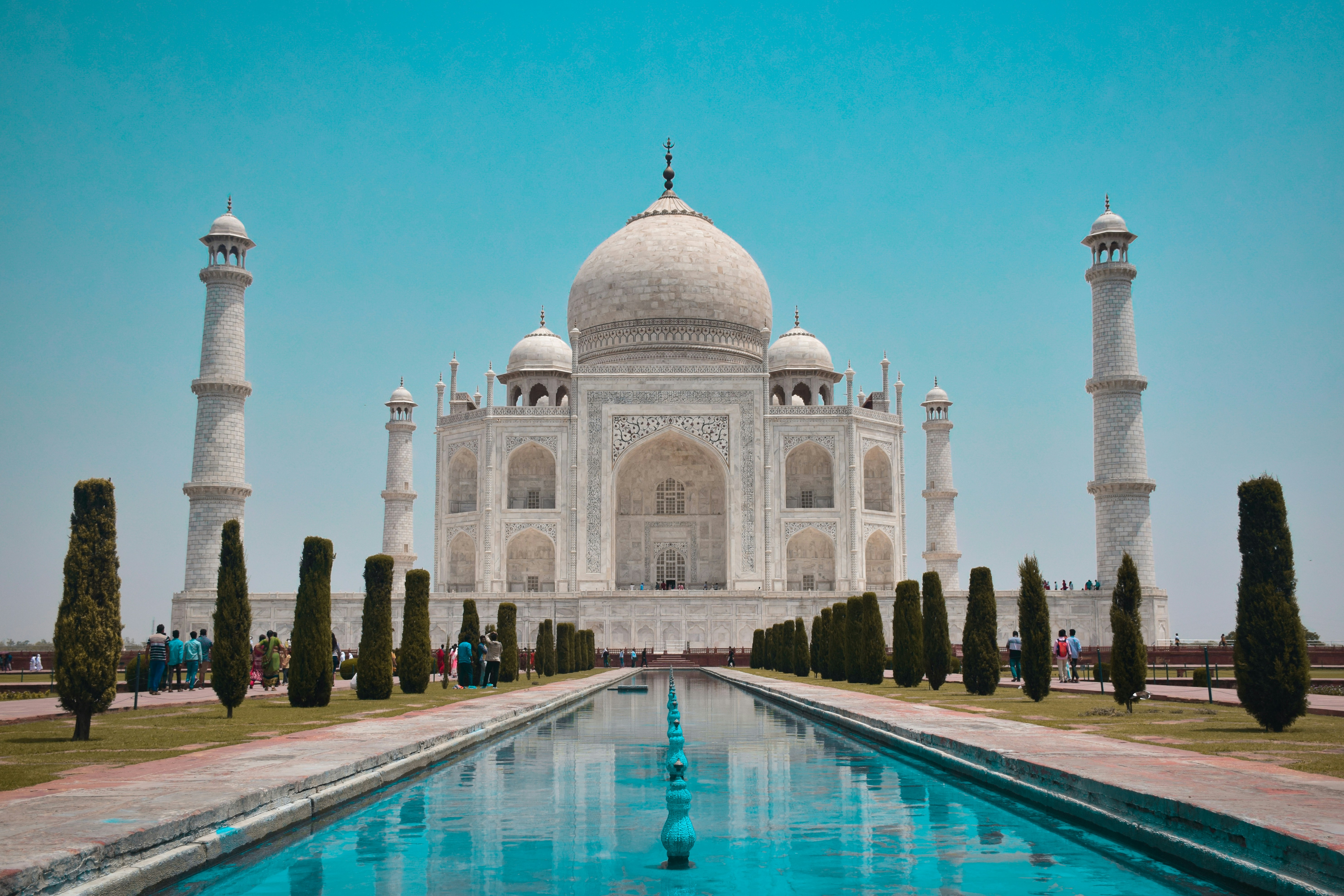The Taj Mahal with its central dome and four minarets, reflecting in a long rectangular pool, under a clear blue sky