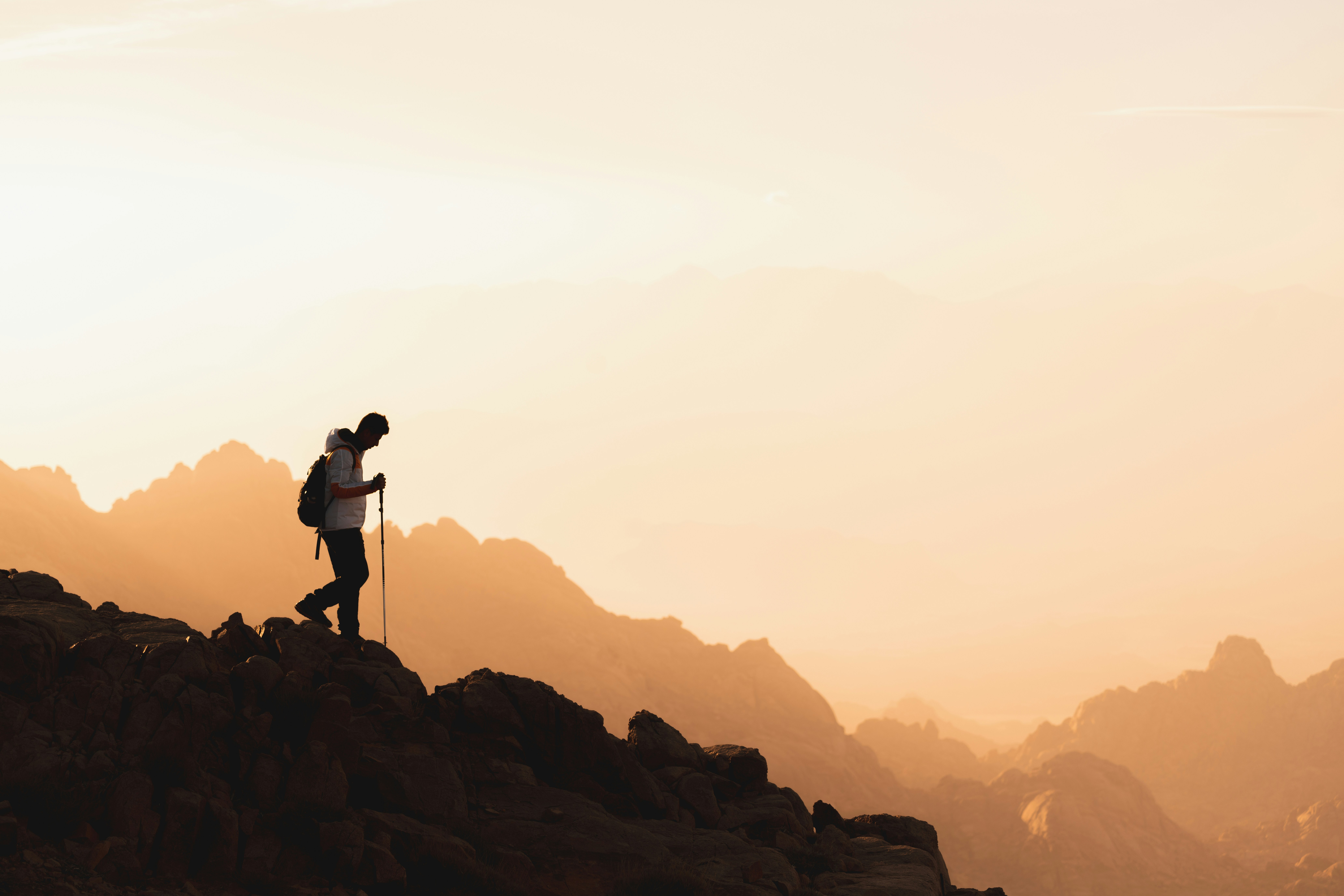 Person hiking on rocky terrain during sunset with mountain silhouettes in the background
